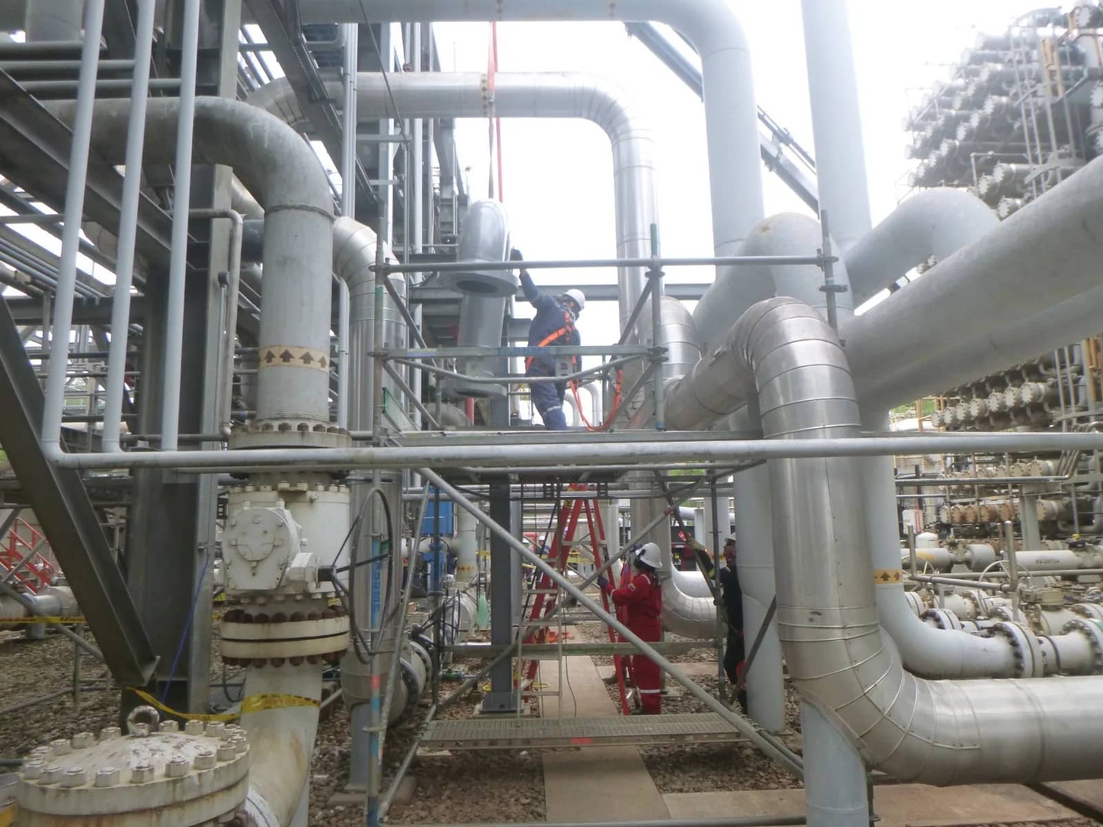 Personal de Ingeniería STM sobre andamio realizando mantenimiento entre líneas de proceso aisladas en una planta.